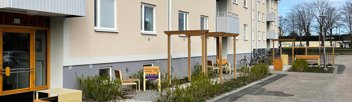 Entrézon vid flerbostadshus med sittplatser, grönska, cykelparkering och tydliga gångstråk som bidrar till ordning, trivsel och hållbar mobilitet i bostadsområdet.