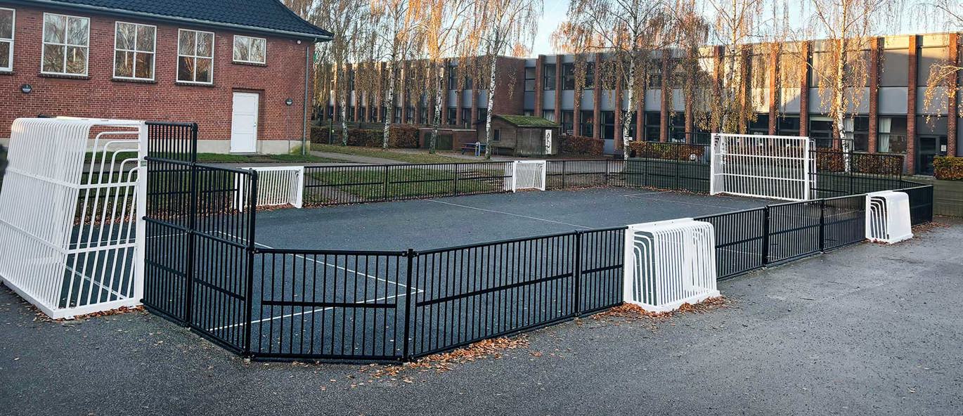 Multibane med sorte bander og hvide mål på langsider og kortsider på asfalt med skole og bygninger i baggrunden