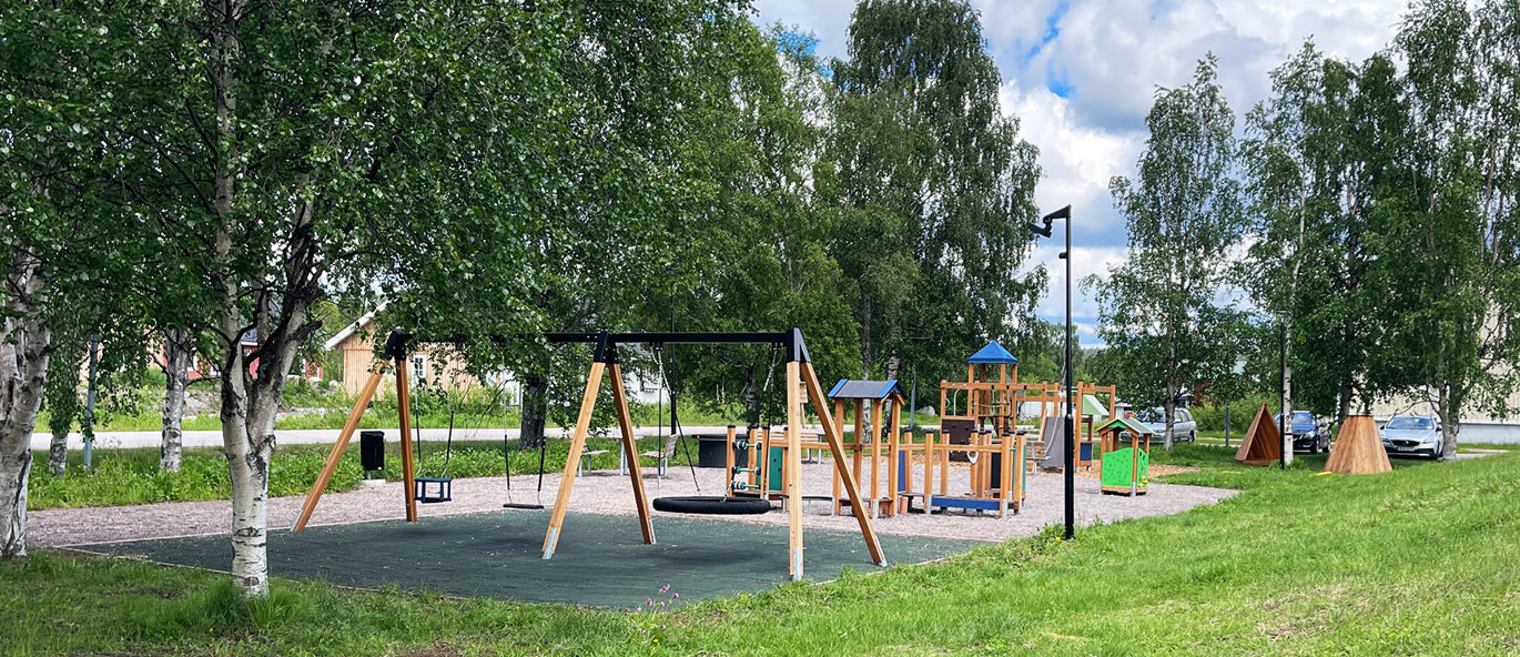 Park med gräs och grus, gungställning och lekställningar.