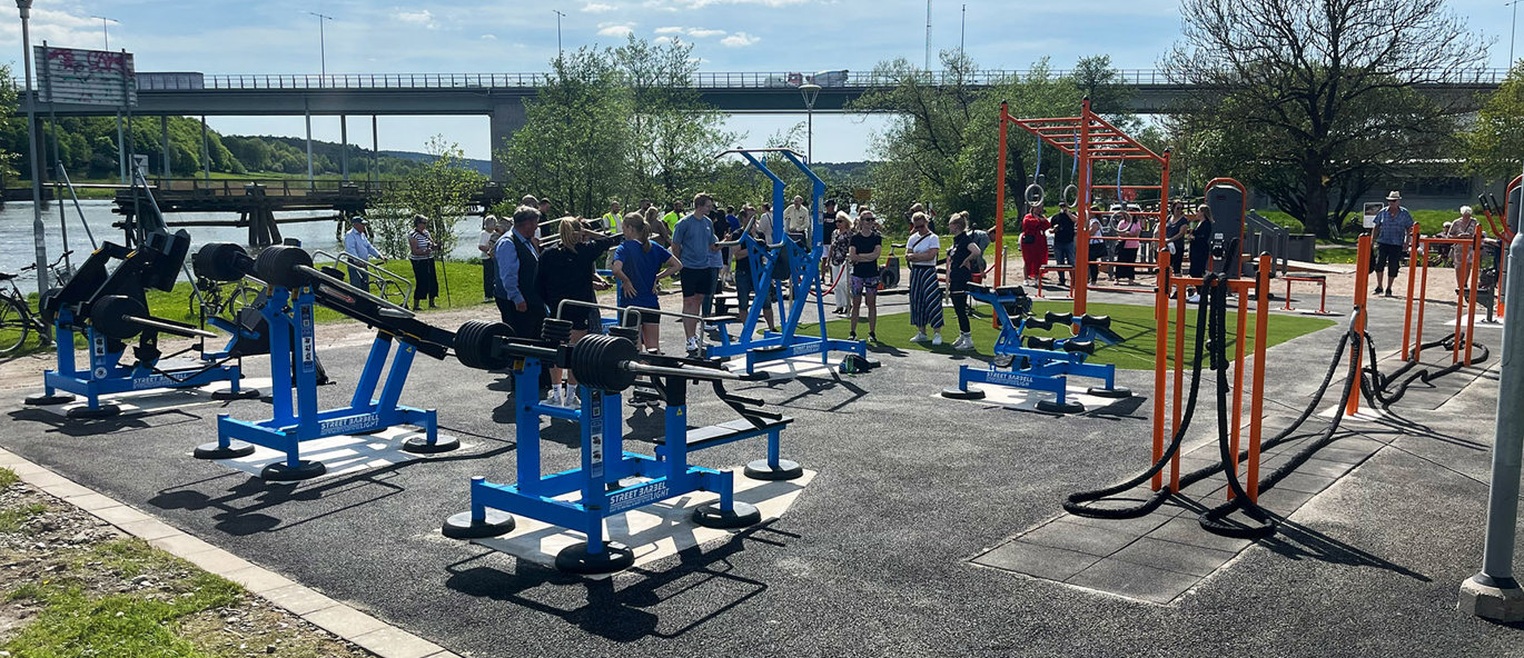 Asfalterad yta med blåa träningsmaskiner och orange träningsställning och battle rope.