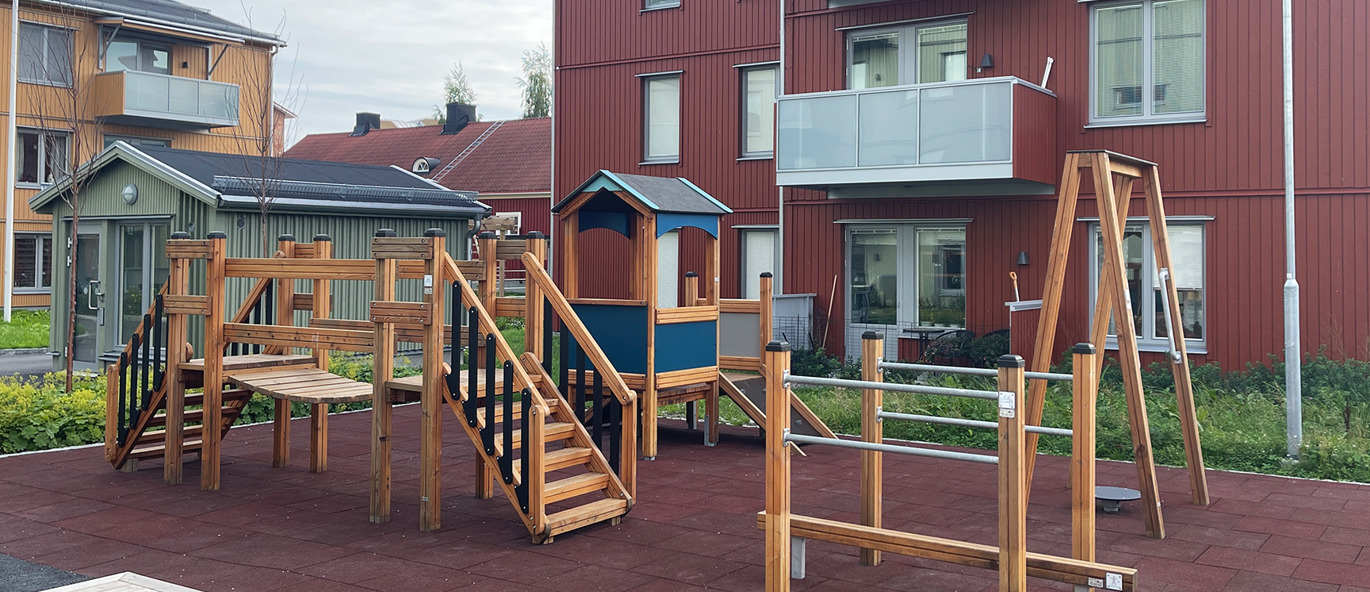 Utegym og lekestativ i tre på rødt fallunderlag i et boligområde.