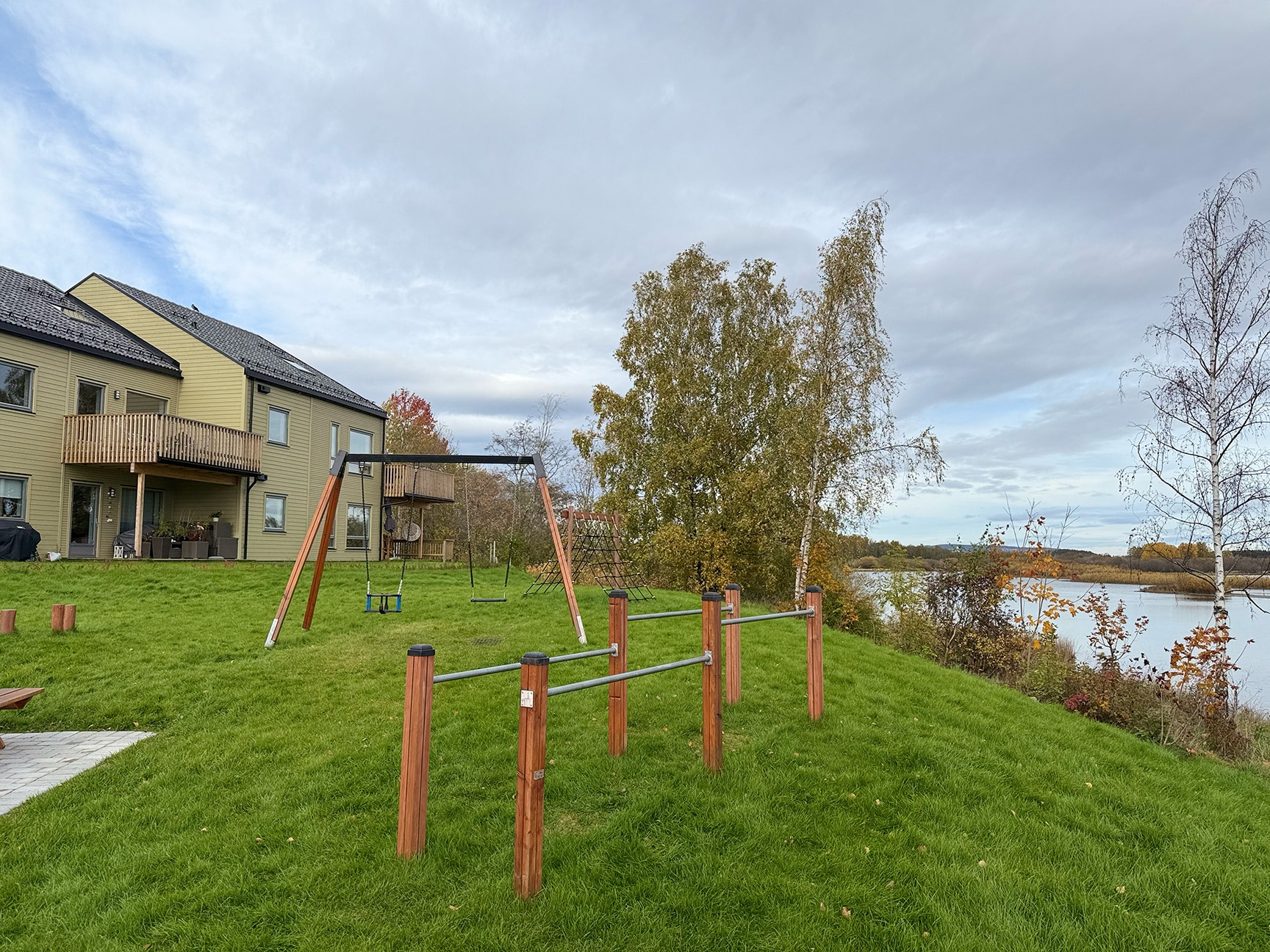 Gungställning och gymnastikbarr på gräsmatta framför hus, med fin utsikt över vattnet.