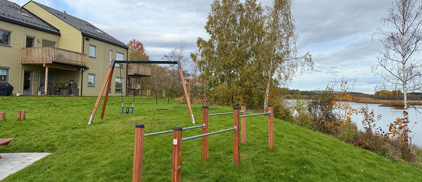 Gungställning och gymnastikbarr på gräsmatta framför hus, med fin utsikt över vattnet.