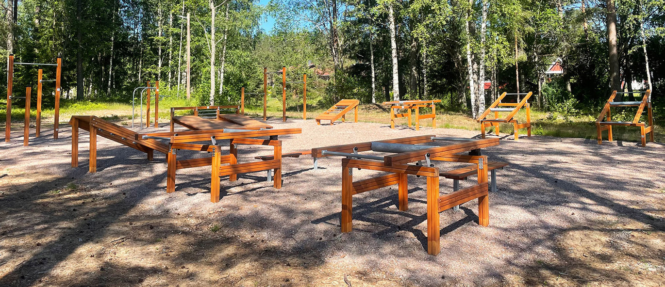 Outdoor fitness med træningsstationer i træ i en lysning omgivet af træer