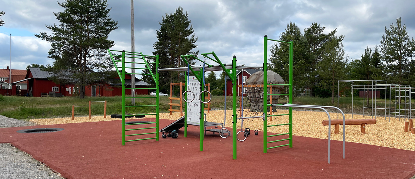 Rött fallskyddsgummi med träningsutrustning och hinderbana samt klättersten i bakgrunden.