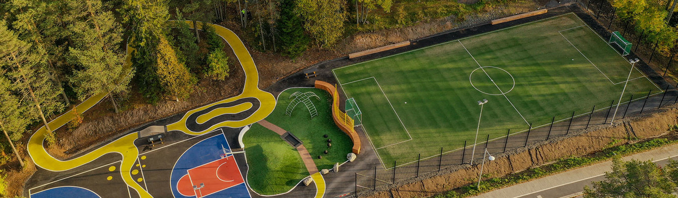 Tillgänglighetsanpassad spontanidrottsplats med basketplaner, konstgräsplan och slingrande gångstråk i parkmiljö sedd ovanifrån.