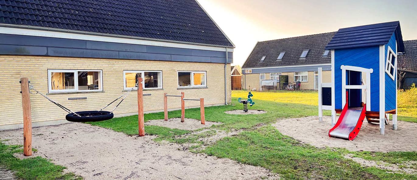 Liten lekeplass med blått lekehus, fugleredegynge, turnstenger og vippehuske
