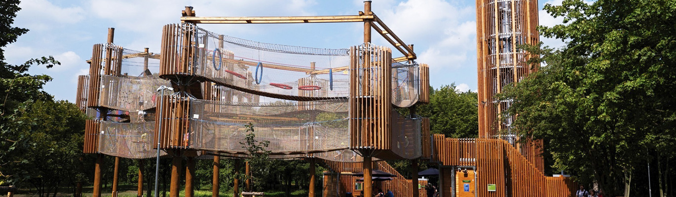 Stor Amaze signaturlekplats i trä med nätlabyrinter och utsiktstorn i parkmiljö – ett arkitektoniskt landmärke för lek och möten.
