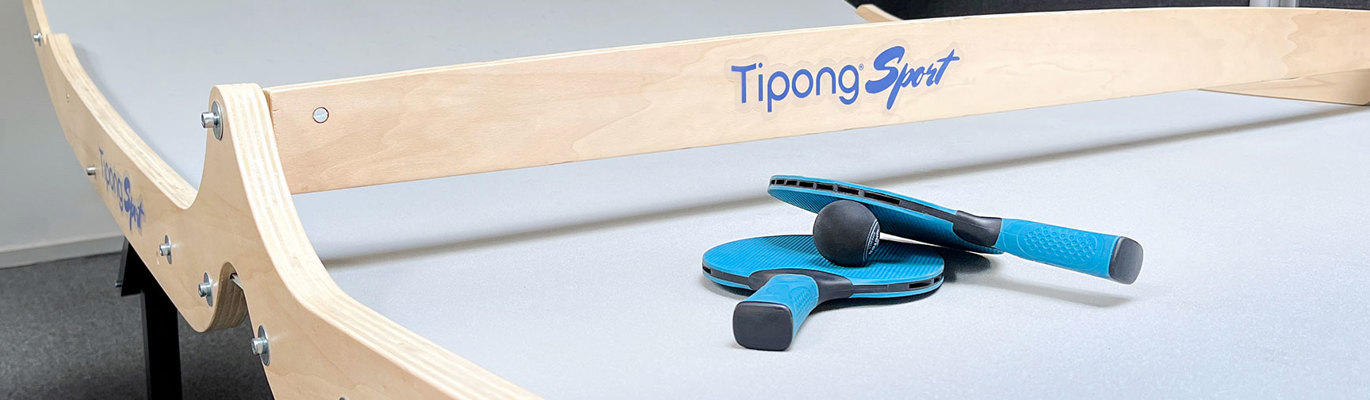 Grått buet spillbord med teksten Tipong Sport i blå og to blå racketer og en svart ball som ligger på bordet