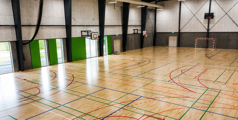 Idrottshall med basketkorgar, handbollsmål och linjer för flera bollsporter
