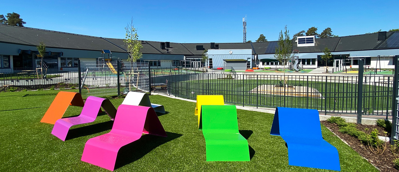 Fargerik skolegård med trampoline, sklie og klatrestativ.