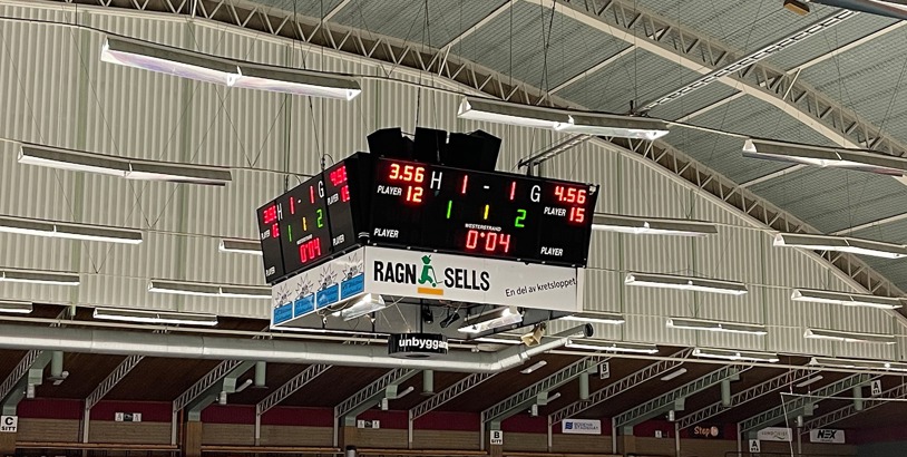 Fyrsidig digital resultattavla med matchtid och resultat upphängd i taket i en idrottshall