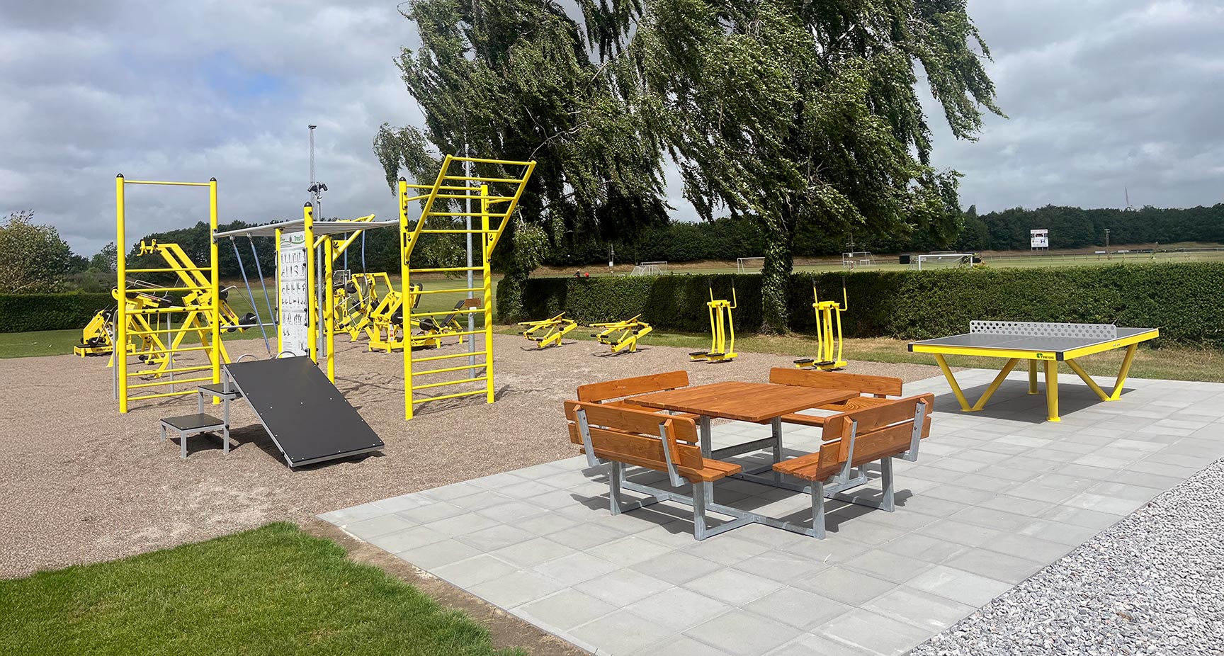 Udendørs fitnessområde ved Torebyhallen med gule træningsredskaber, Street Barbell-anlæg, bordtennisbord og opholdsområde.