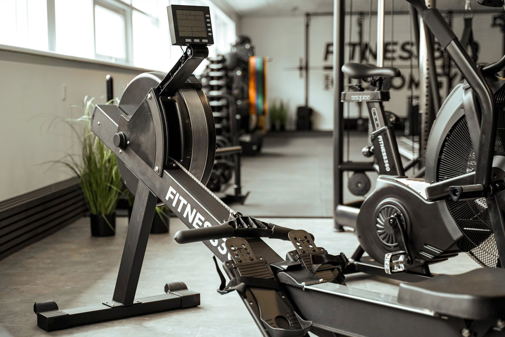 Nærbillede af Fitness360 romaskine og airbike i træningsmiljø med mere træningsudstyr i baggrunden
