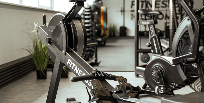 Träningsutrustning från Fitness360 i gymmiljö med roddmaskin och airbike för konditionsträning