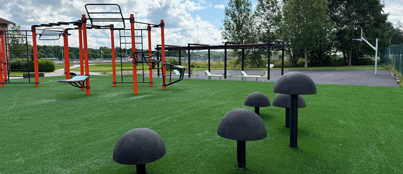 Grön konstgräsmatta med ninja stolphopp, en orange träningsställning och en pergola i bakgrunden.