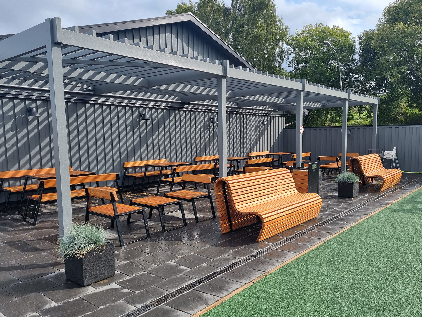 LEPUS bord, soffor och stolar under en grå pergola på en rastplats i Gränna, med Wave-parksoffor och planteringskärl framför sittgrupperna.