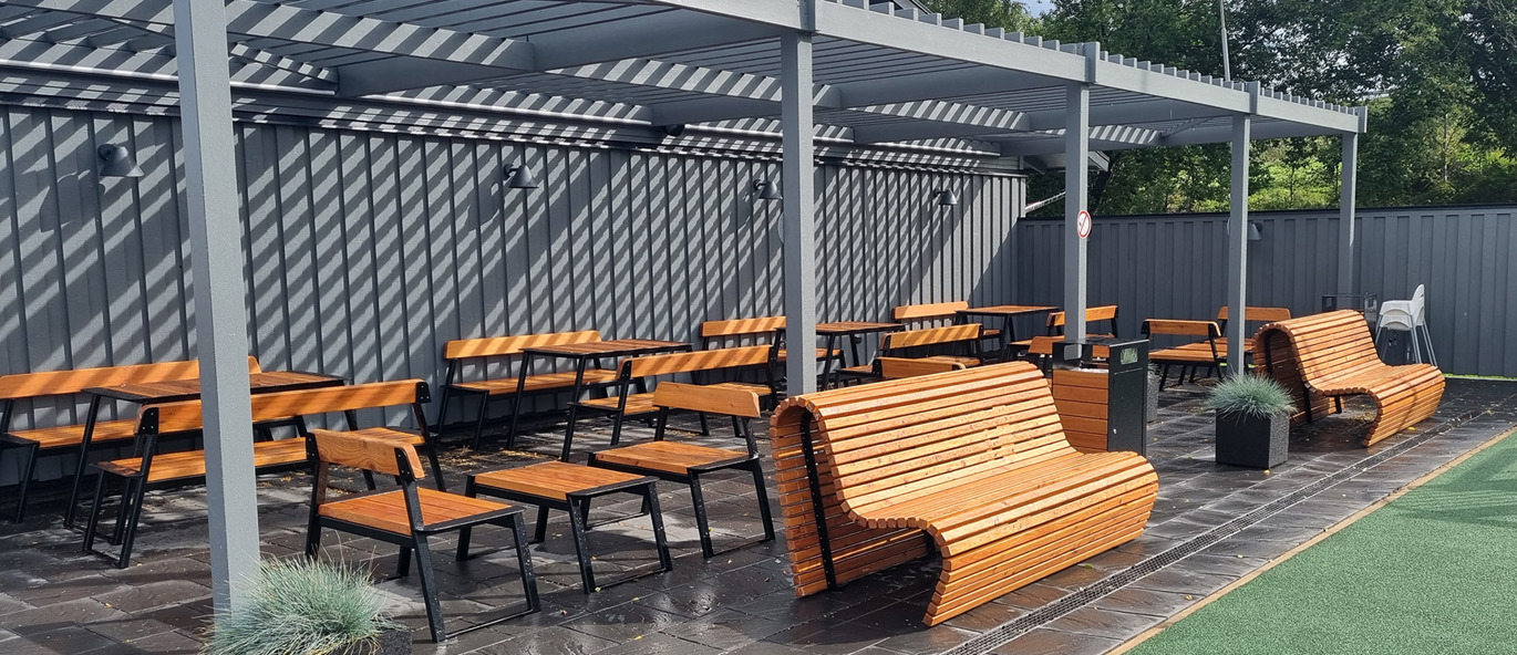 LEPUS bord, benker og stoler under en grå pergola på en rasteplass i Gränna, med Wave parkbenker og plantekasser foran sittegruppene.