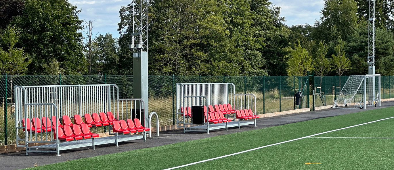 Sittplatsläktare med röda stolar intill den nya konstgräsplanen på Skarpans IP i Linköping.