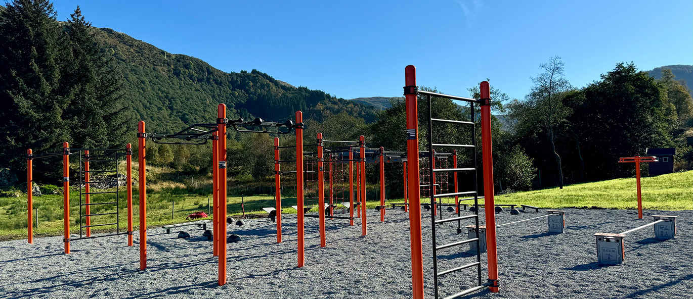 Orange klätterställning och träningsställning på grusplan med skog bakom.