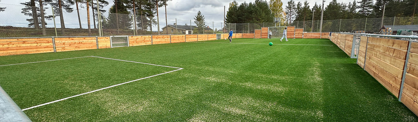 Multiarena med konstgräs, träsarg och flera användare i aktivitet på en skolgård i utomhusmiljö.