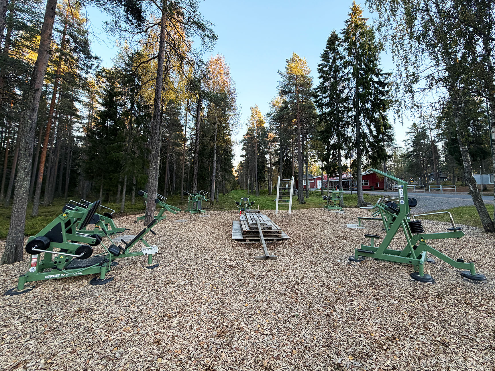 Utegym på Ormberget i Luleå med gröna Street Barbell Light-träningsmaskiner placerade mellan höga träd i friluftsområdet.