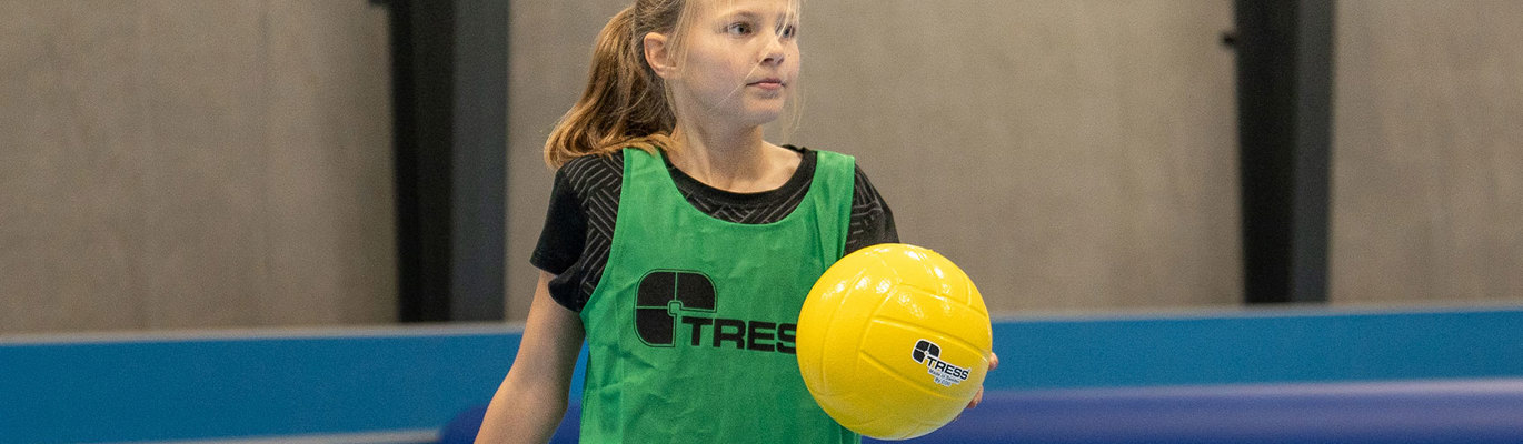 Jente med overtrekkstrøye på og ball i hånden i en gymsal