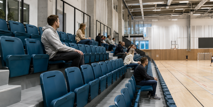 Blå läktarstolar med åskådare i en modern idrottshall