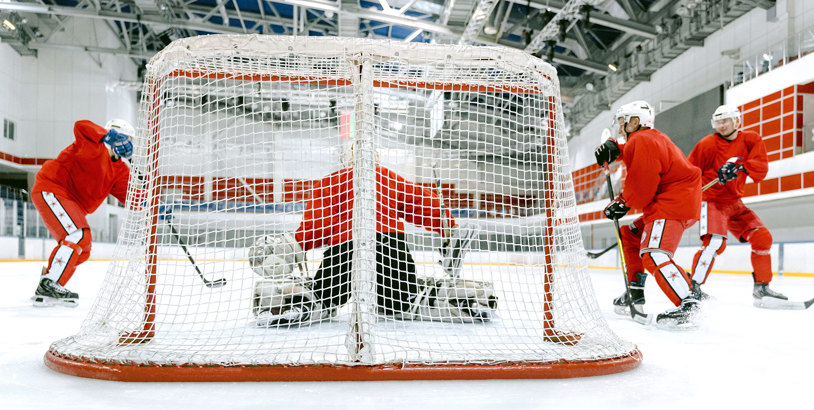 Ett hockeymål på isen med flera hockeyspelare med röda kläder