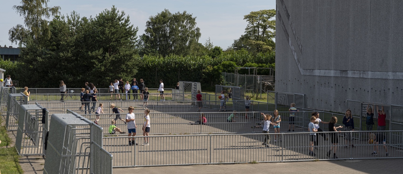 Barn leker og er aktive på et inngjerdet aktivitetsområde ved en skole i Vejle. Området kombinerer multisportflater med åpne soner for lek, aktivitet og bevegelse utendørs, og skaper et inkluderende møtepunkt for elever i alle aldre.
