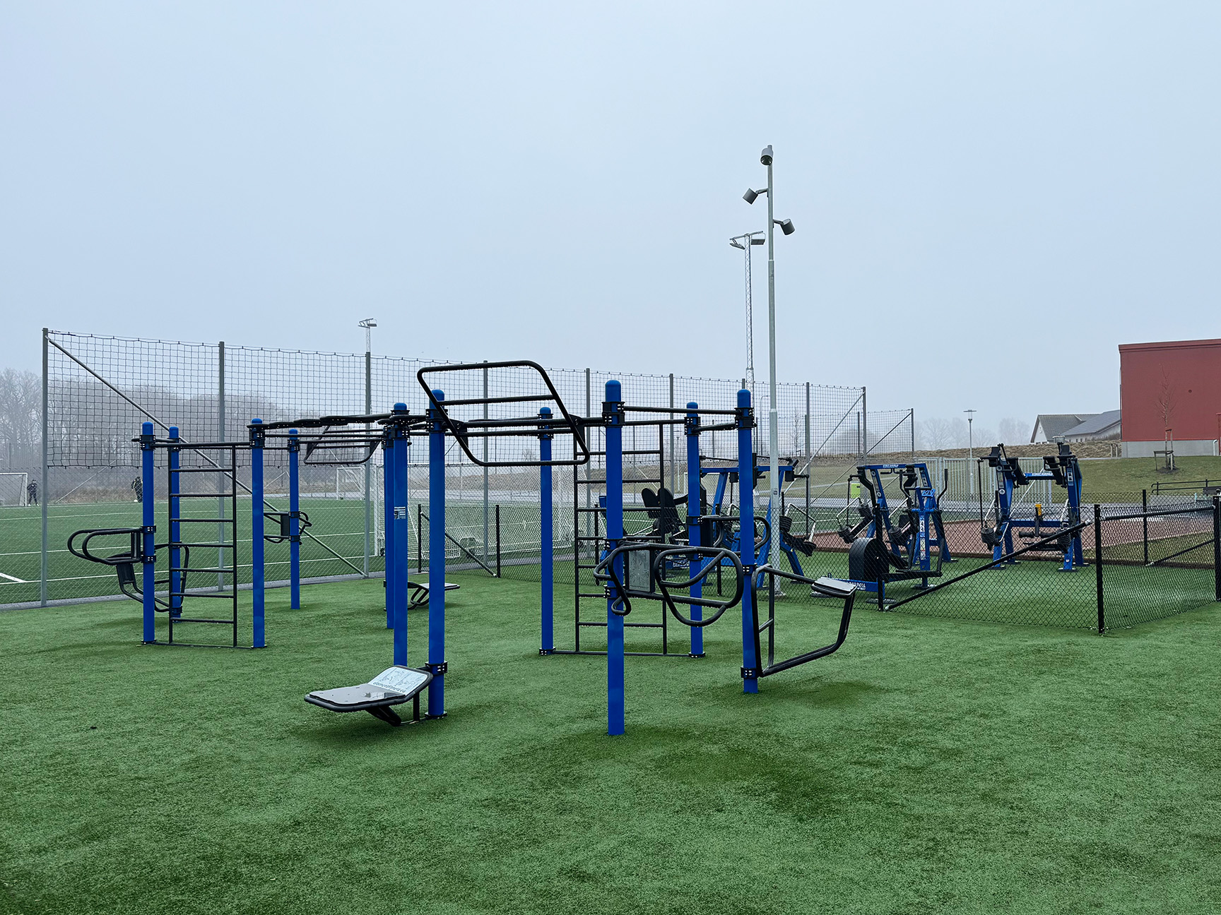 Blå träningsställning och blåa träningsmaskiner på en grön gräsmatta vid en idrottsplats.