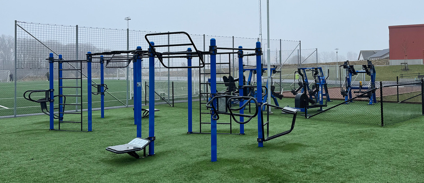 Blå träningsställning och blåa träningsmaskiner på en grön gräsmatta vid en idrottsplats.