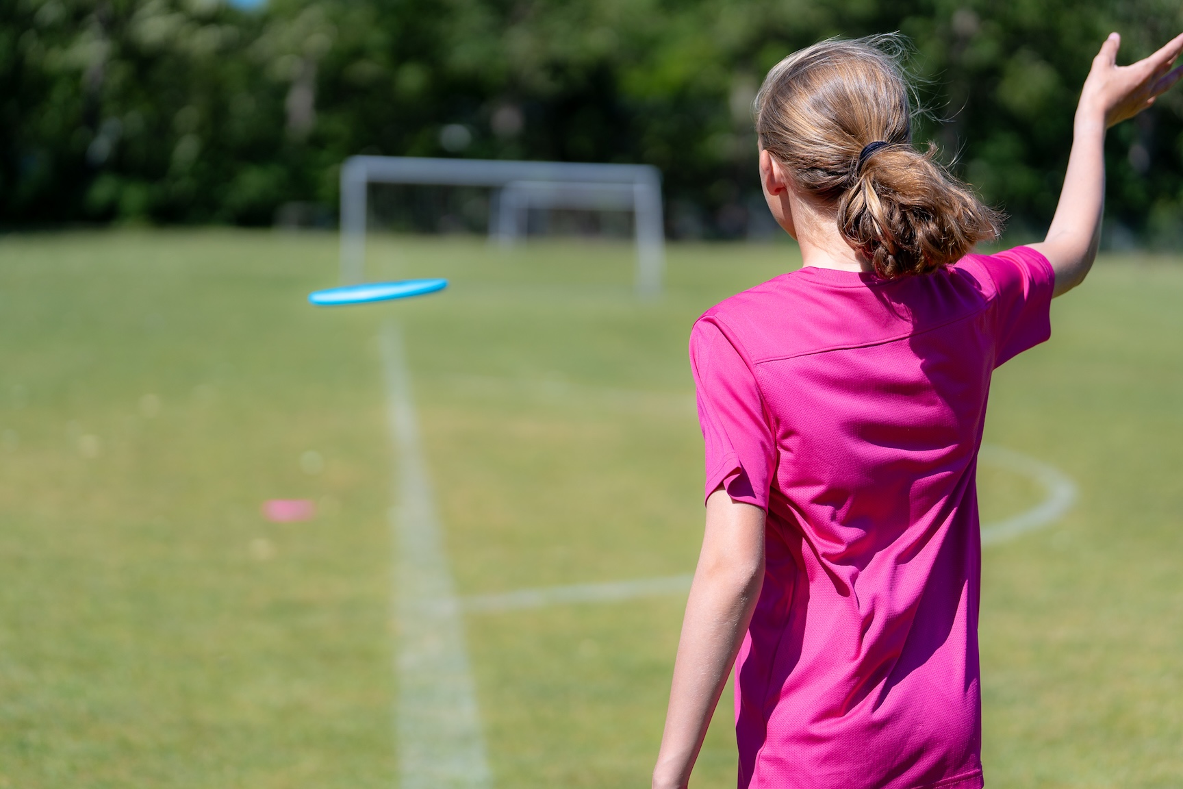 Pige spiller discgolf i et grønt område ved skole