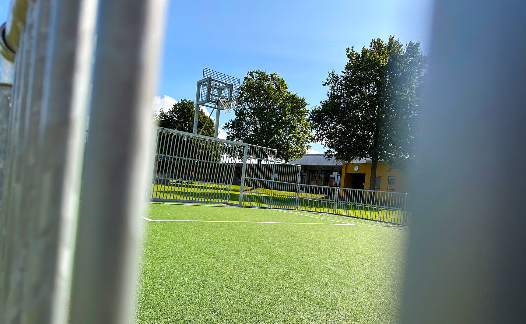 Multibane i stål med basketballtop og grønt kunstgræs fotograferet gennem banderne