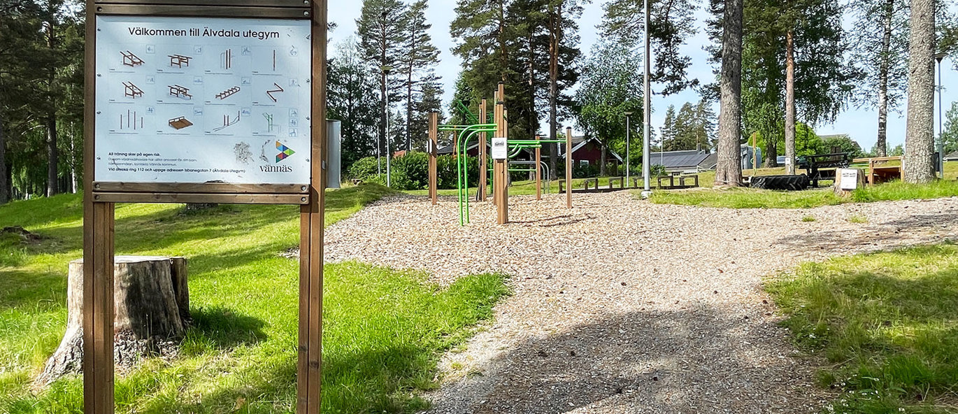 Informasjonsskilt med illustrasjoner av treningsstasjoner i en park med utegym og ulike treningsapparater.
