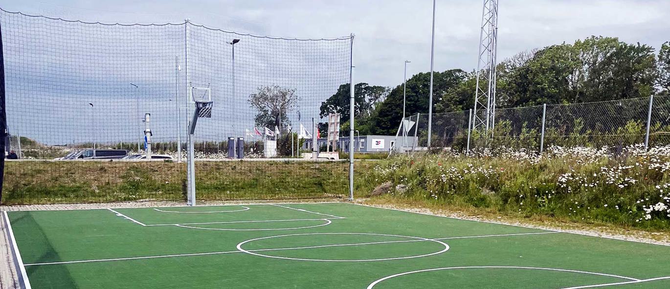 Basketballbane med grønt dekke og varmgalvanisert basketstativ i et boligområde.
