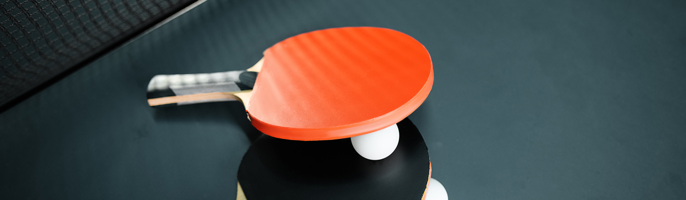 to bordtennisracketer i svart og rød som ligger på et bordtennisbord sammen med en bordtennisball