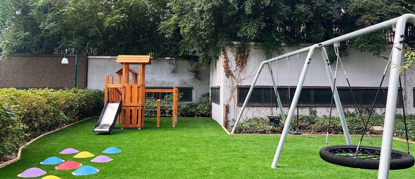 Grön gräsmatta med färgglada balanskulor, en klätterställning av trä och en gungställning av stål.