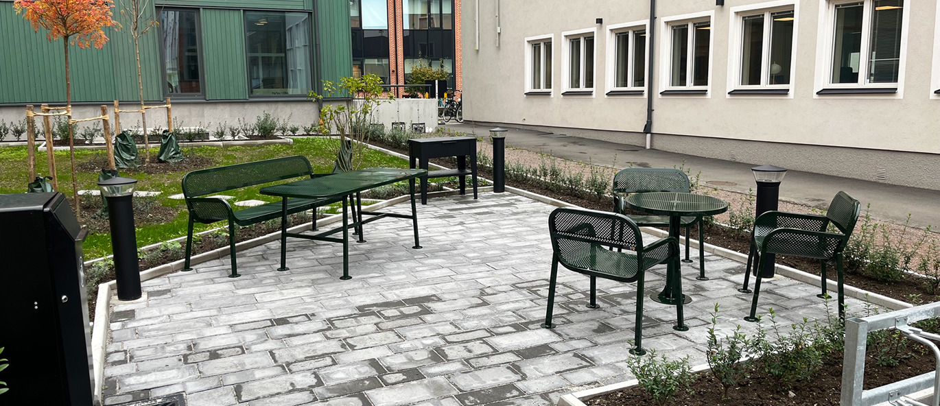 Mörkgröna BISTRO parkmöbler med bord, stolar och soffor på en nyanlagd uteplats i bostadsområde i Linköping.