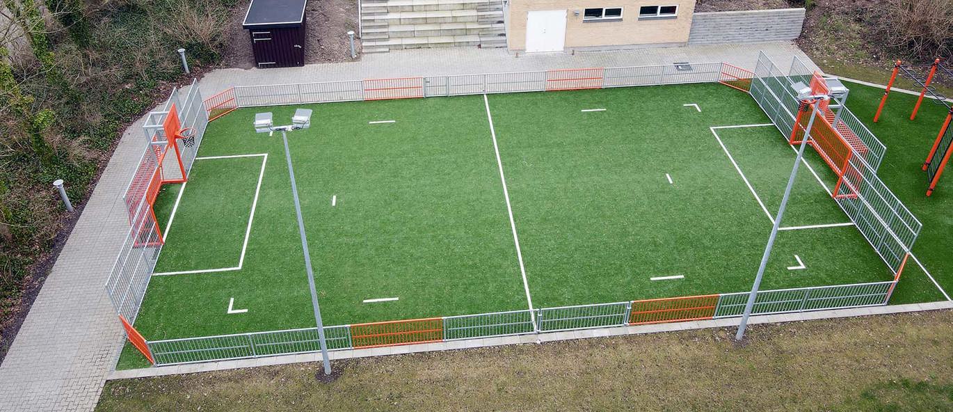 Multiarena av grått och orange stål med grönt konstgräs.