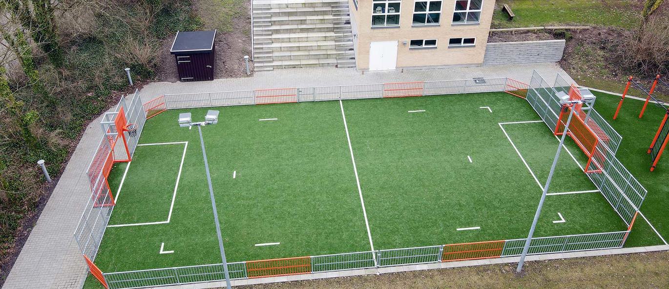 Multibane med grått og oransje stål med grønt kunstgress.