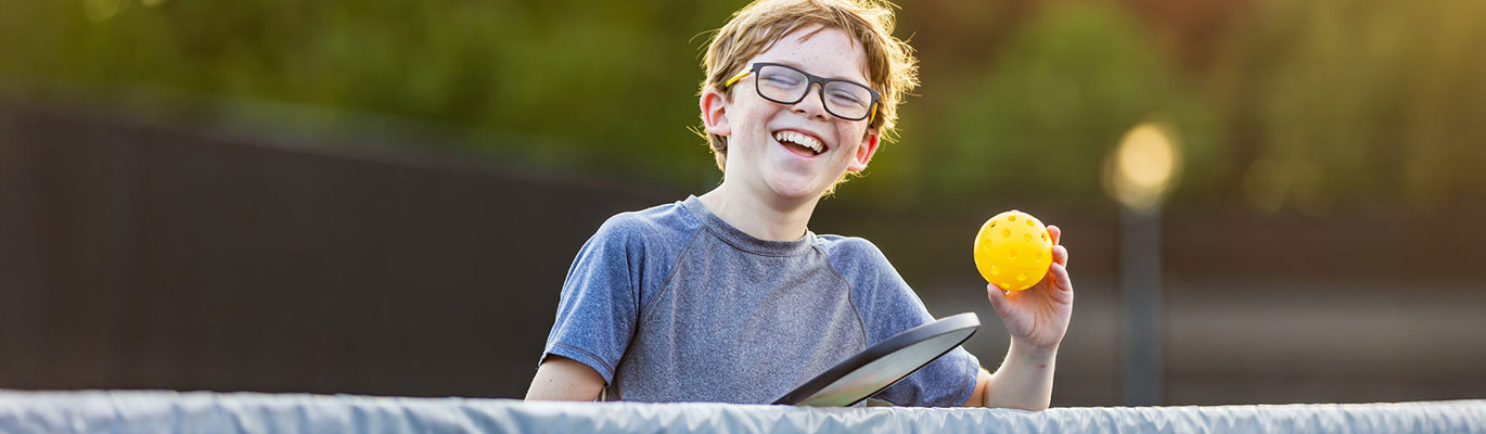 Smilende gutt som spiller pickleball utendørs