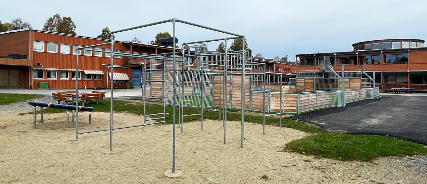 Parkour-ställning på grusunderlag framför en multiarena och där bakom en röd skolbyggnad.