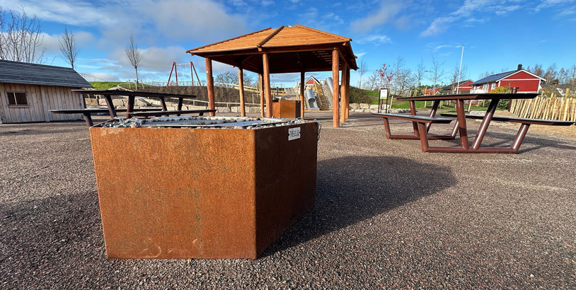 Utendørs møtested med parkgrill i cortenstål, bålhus i tre og bord- og benkesett.