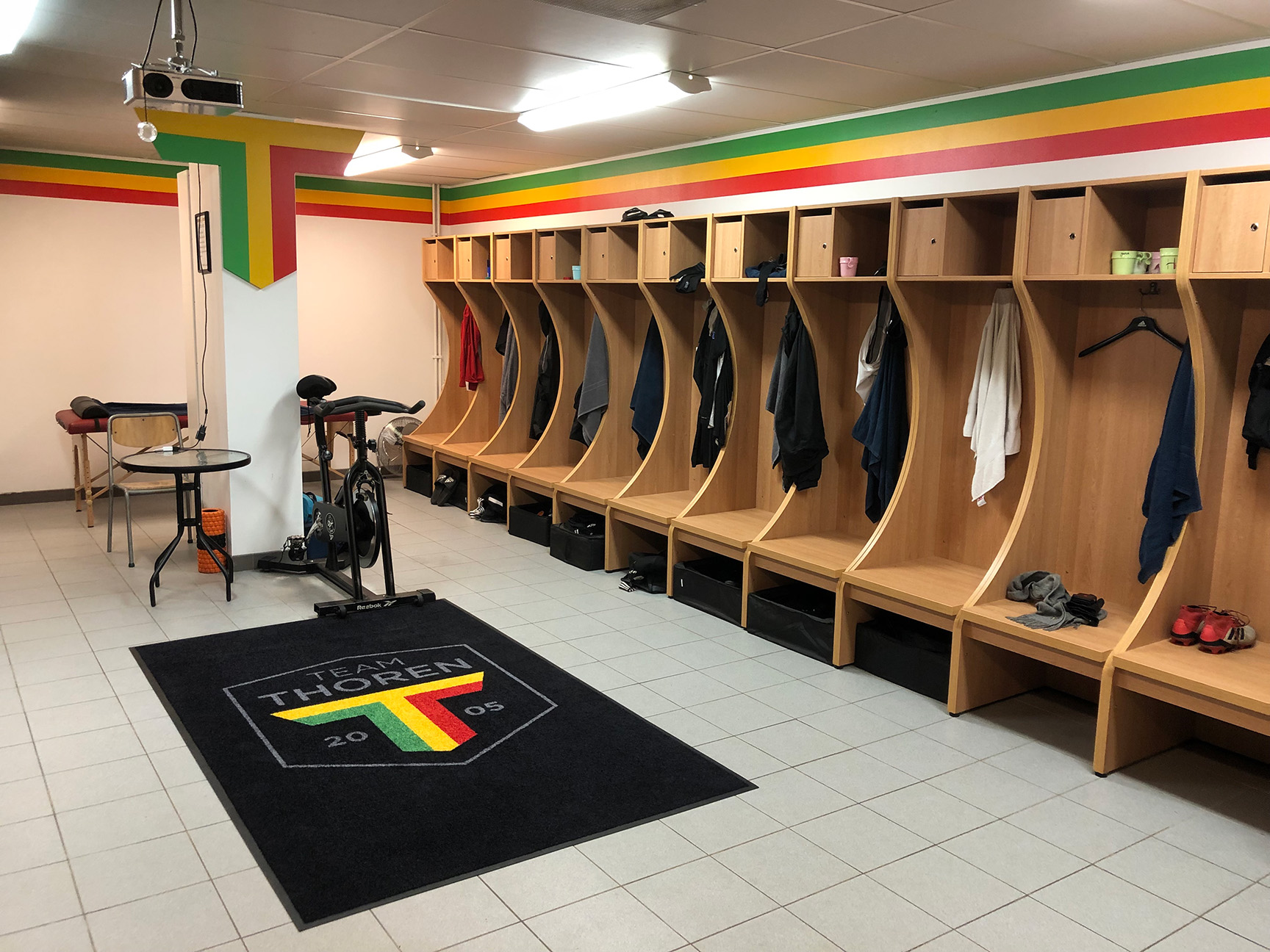 Omklädningsrum för Team TG FF i Umeå med träbås, individuella förvaringsplatser och klubbfärger i grönt, gult och rött på väggarna.