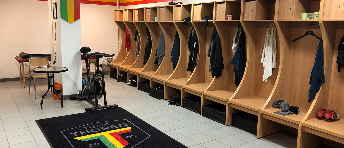 Garderoberom for Team TG FF i Umeå med garderobebåser i tre, individuelle oppbevaringsplasser og klubbfarger i grønt, gult og rødt på veggene.