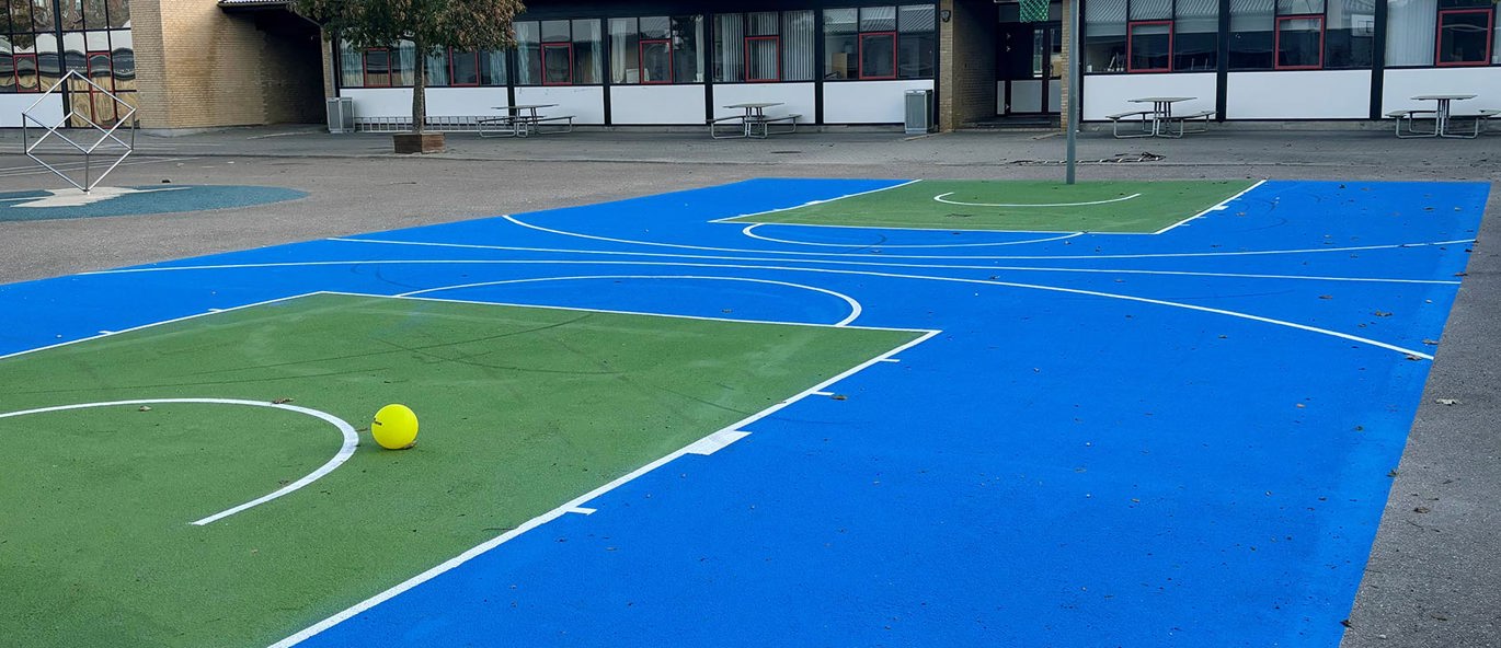 Oppmerket basketballbane i blå og grønne farger i skolegården