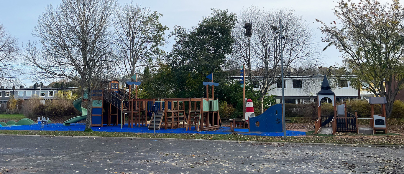 Lekplats i en park med blått underlag, en stor lekbåt samt en borg med ramper.