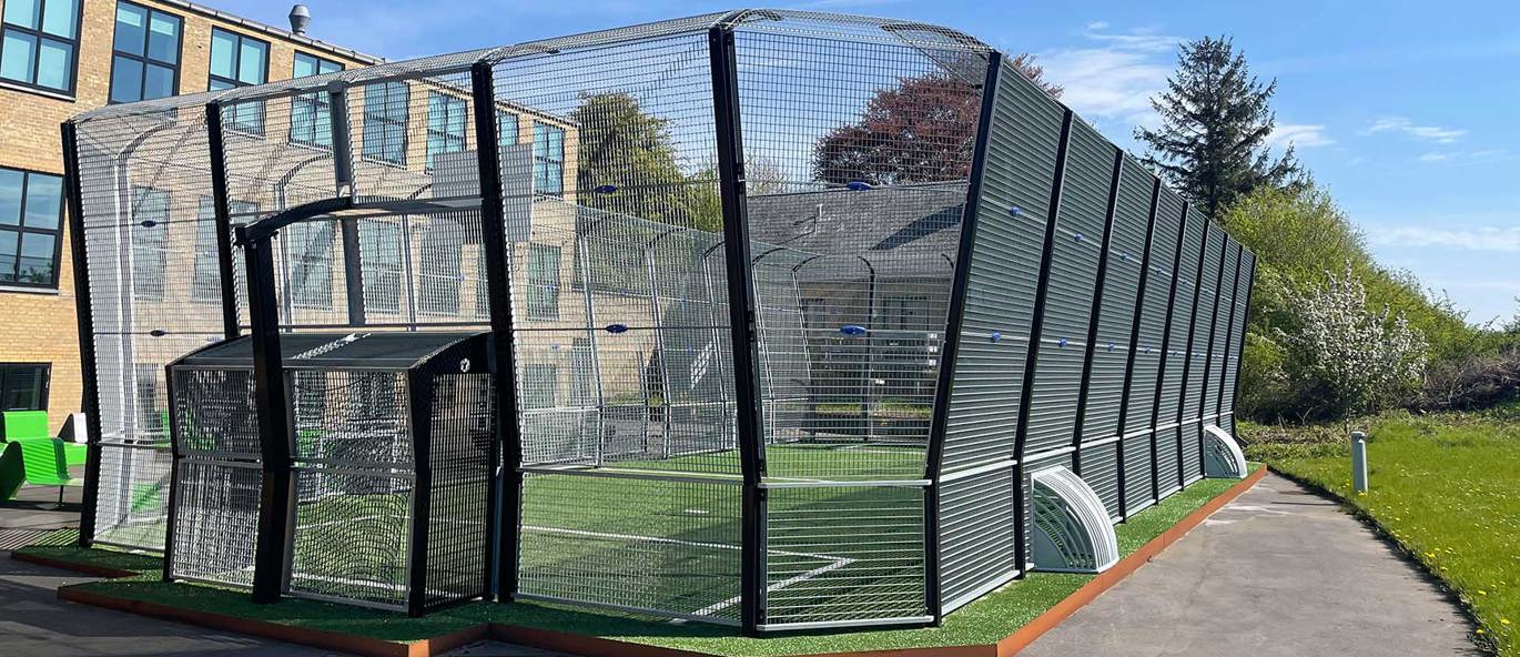 Stor multibane foran skole med grønt kunstgræs, kantafskærmning og sorte bander