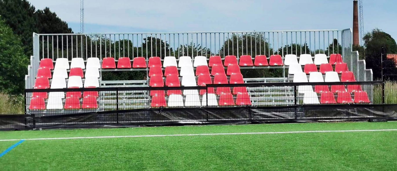 Tribune med røde og hvite tribuneseter på idrettsanlegg i Præstø.